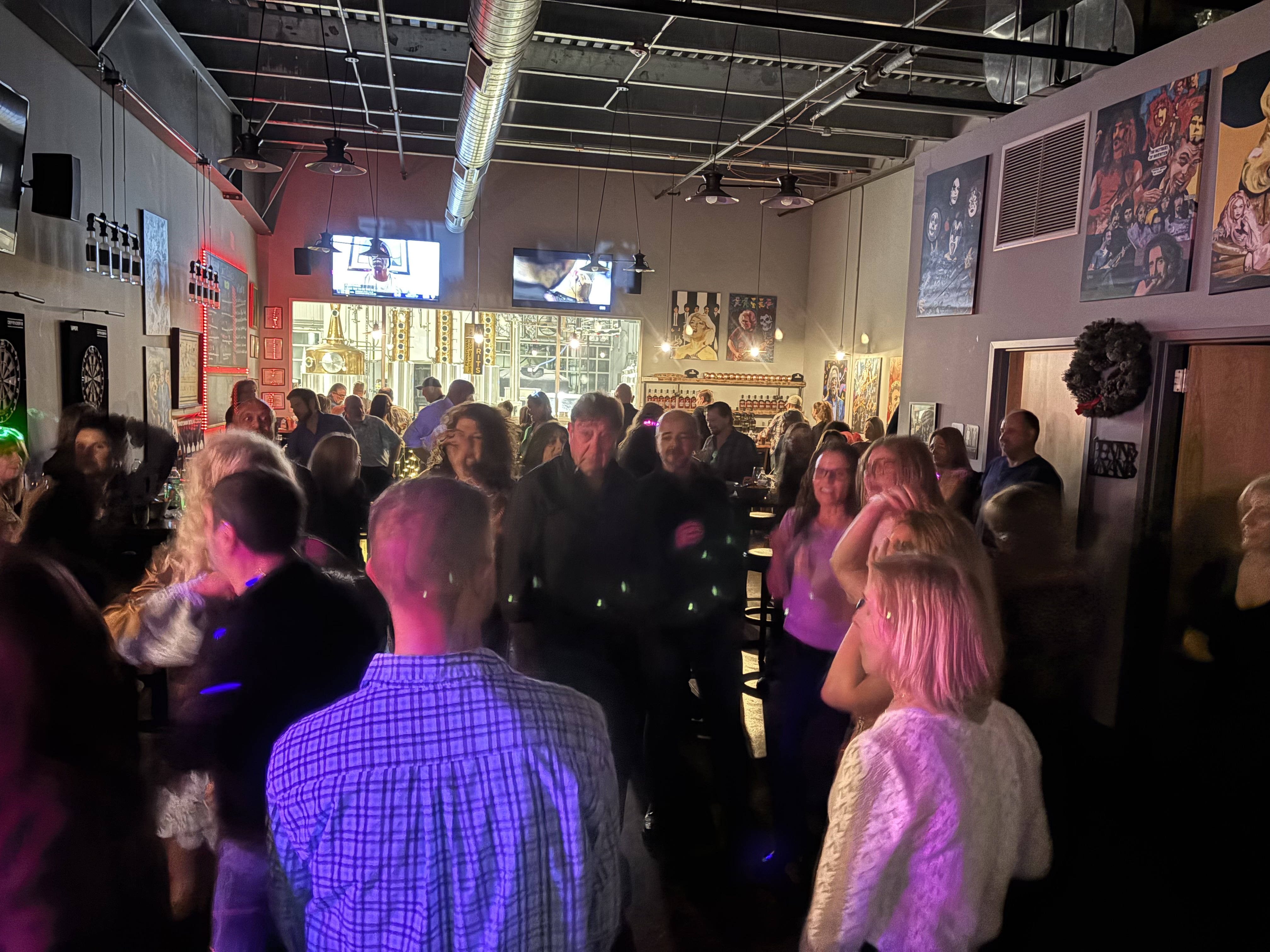 Guests mingling and dancing in a lively venue with purple lighting and artwork on the walls