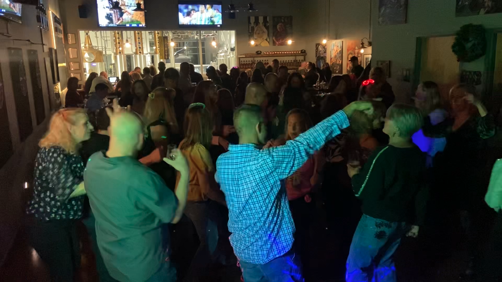 Packed dance floor with guests dancing under green and blue lights
